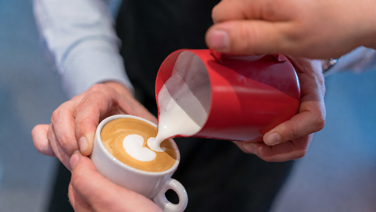Latte Art eingießen: Milch aus einem roten Kännchen fließt in eine Espressotasse