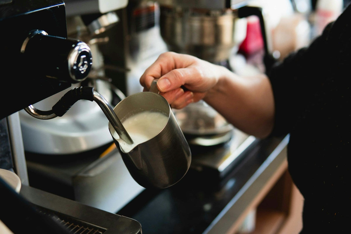 Milch wird mit der Dampflanze im Edelstahlkännchen aufgeschäumt