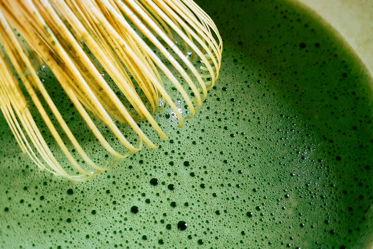 Leuchtend grüner Matcha wird mit einem Bambusbesen aufgeschlagen